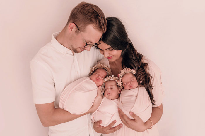 Suesse Drillinge liegen im Arm der Eltern beim Neugeborenen Shooting in Duesseldorf fotografiert von Babyfotografin