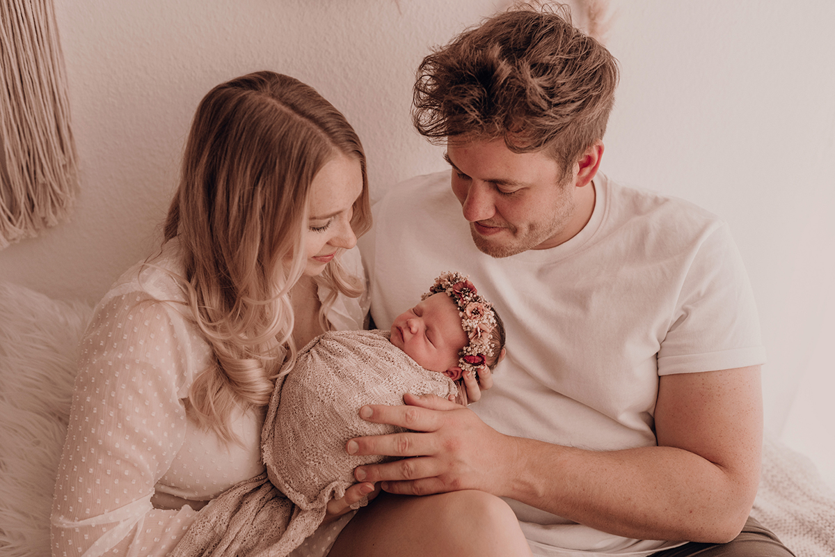 Familie guckt verliebt ihr Neugeborenes Baby an bei Neugeborenenshooting mit Babyfotografin Laura Stecher