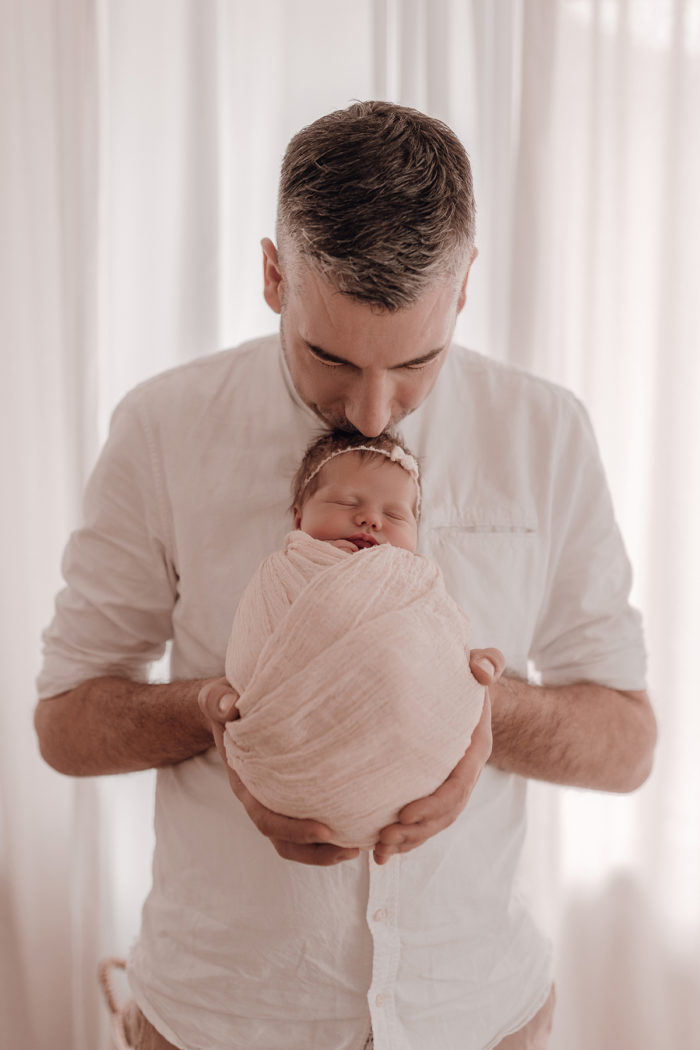 Papa küsst Baby beim Neugeborenen Shooting, Geschwisterliebe, Familienshooting bei einfallslicht fotografie in Düsseldorf, Baby, Babykleidung, Babybody